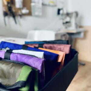 Detailaufnahme von fertigen Hip Bags in verschiedenen Farben. Im Hintergrund eine Nähmaschine.